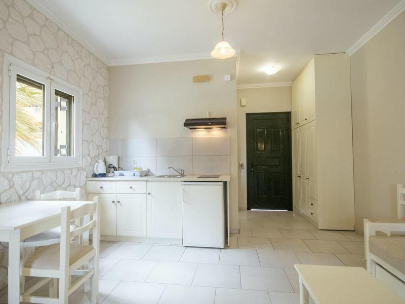 Kleine, helle Küche mit weißer Einrichtung, Tisch, Stühlen und grünem Eingangstür im Hintergrund.