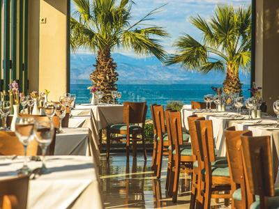 Offenes Restaurant mit gedeckten Tischen und Blick auf Palmen und das Meer.