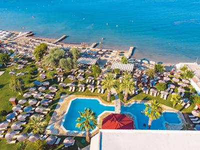 Luftaufnahme eines Urlaubsresorts mit Pool, grünen Gärten und Strand am Meer.