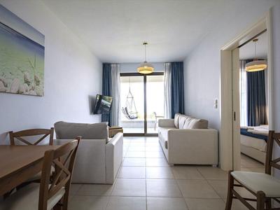 Helles Wohnzimmer mit weißen Sofas, Holz-Esstisch, Flachbild-TV und großem Fenster zum Balkon.