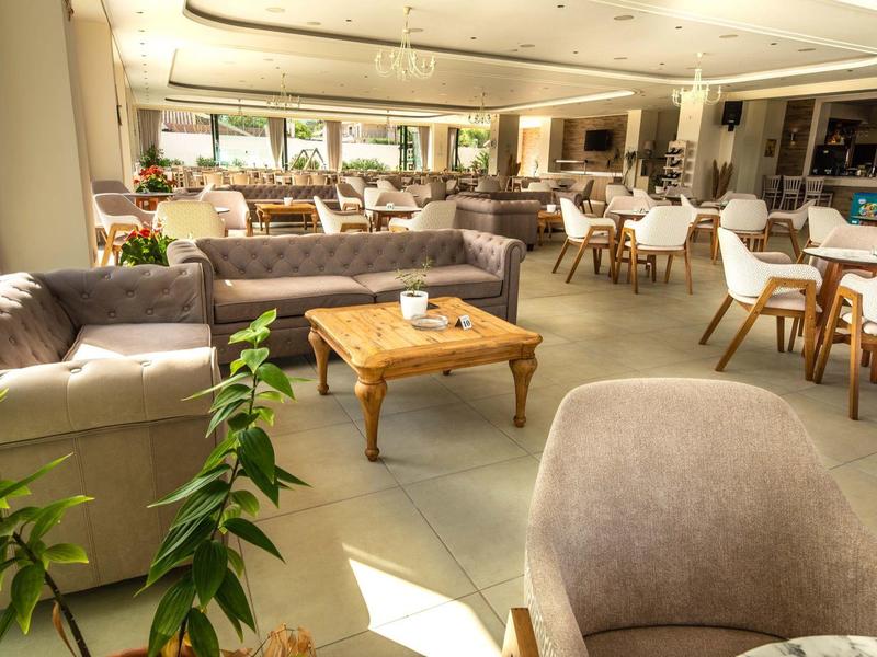 Heller, moderner Gastraum mit bequemen Sofas, Holztischen und Pflanzen am Sonnentag.