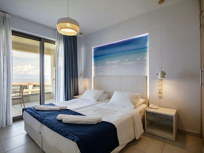 Modernes Schlafzimmer mit Doppelbett, blauen Vorhängen und Zugang zu Balkon mit Meerblick.