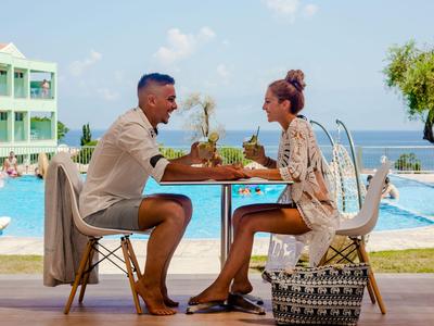 Couple sitting at table overlooking pool and sea, enjoying a meal together.