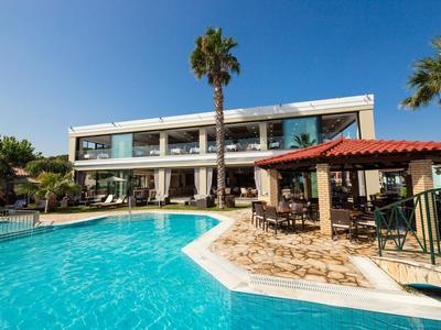 Modern hotel with large windows, palm trees, and a clear blue outdoor swimming pool.