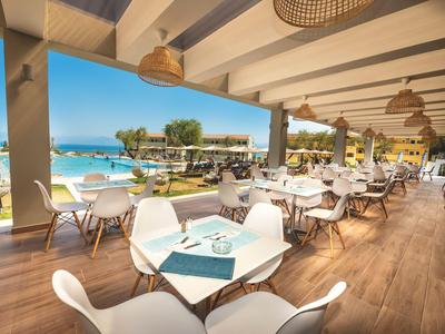Open restaurant with white tables and chairs overlooking pool and sea under sunny skies.
