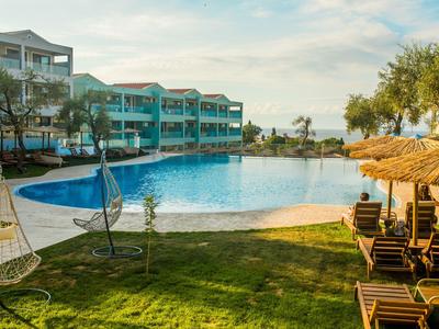 Hotel pool area with hanging chair and sun loungers on grass with buildings in the background