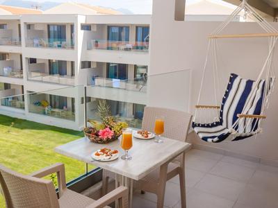 Balcony with table, chairs, and hanging chair overlooking modern hotel rooms and garden.