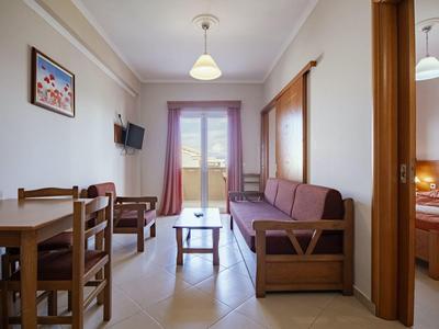 Heller Wohnraum mit Holzmöbeln, großem Fenster und angrenzendem Schlafzimmer mit Doppelbett.