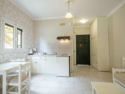 Kleine, helle Küche mit weißer Einrichtung, Tisch, Stühlen und grünem Eingangstür im Hintergrund.