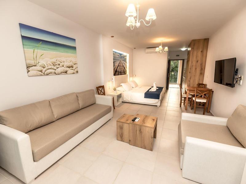 Helles Zimmer mit beiger Sitzgarnitur, Holztisch, Bett, Schreibtisch und Meeresbild an der Wand.