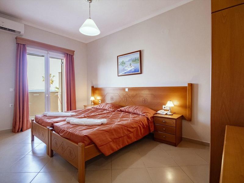 Schlichtes Schlafzimmer mit Doppelbett, roten Decken, Nachttischlampen und großem Fenster mit Vorhängen.