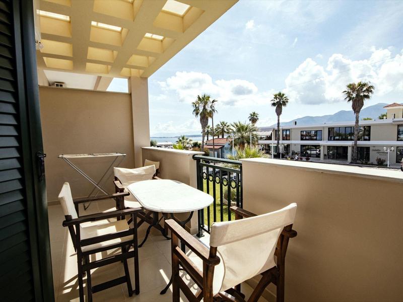Balkon mit weißem Tisch, vier Stühlen, überdacht, Blick auf Palmen und Gebäude bei blauem Himmel.