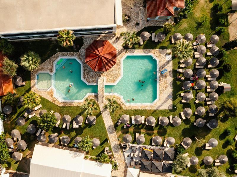 Luftaufnahme eines Pools mit Liegestühlen und Sonnenschirmen in einem Hotelresort.