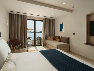 Camera d'hotel moderna con letto matrimoniale, area salotto e vista sull'acqua attraverso finestre a tutta altezza.