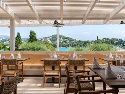 Terrazza aperta con tavoli e sedie in legno, vista su colline verdi e montagne.