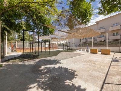 Un ingresso moderno con strutture d'ombra, panchine e edifici sullo sfondo in una giornata di sole.