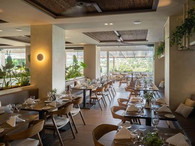 Ristorante moderno con tavoli e sedie in legno, grandi finestre e piante.