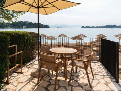 Terrasse mit Holztisch und Stühlen unter Sonnenschirm mit Blick auf ruhigen See und Sonnenschirme am Ufer