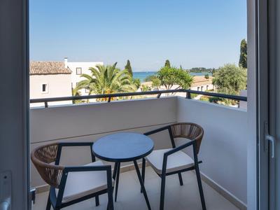 Balkon mit zwei Stühlen und kleinem Tisch, Blick auf Palmen und Meer am Horizont.