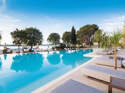 Großer Pool mit Liegen umgeben von Bäumen und Blick aufs Meer bei klarem Himmel.