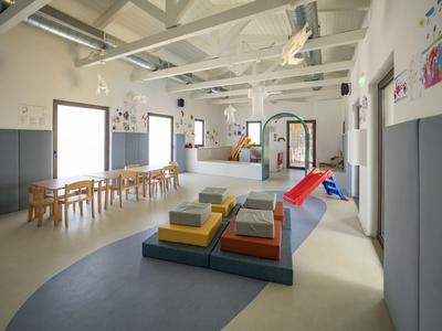 Heller, moderner Kindergartenraum mit Spielbereich, Tischen und bunten Sitzkissen.