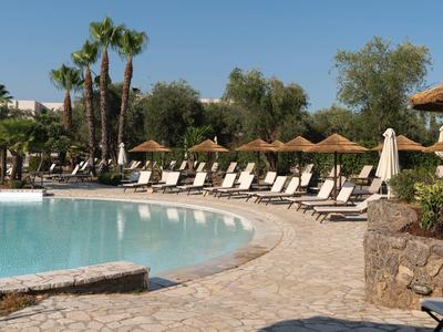 Pool area with lounge chairs, umbrellas, and palm trees under clear sky at a resort.