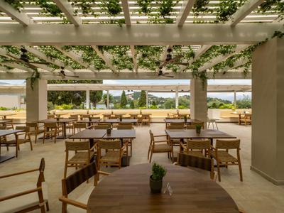 Covered outdoor terrace with tables and chairs, view of garden and sea in the background.