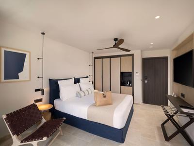 Camera d'albergo moderna con letto grande, sedia, ventilatore a soffitto e TV.