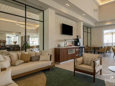 Area lounge elegante dell'hotel con divani comodi, poltrone e una TV moderna a parete.