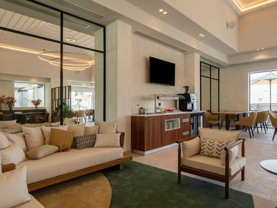 Lobby dell'hotel moderna con posti a sedere confortevoli, TV, macchina del caffè e grandi finestre.