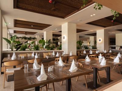 Ristorante moderno con tavoli in legno, tovaglioli bianchi e piante verdi all'interno.