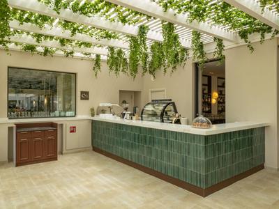 Area bar esterna moderna con piastrelle verdi e piante pendenti sotto un pergolato.