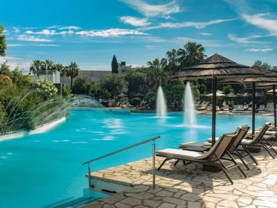 Pool area with loungers, water fountains, and palm trees under a blue sky