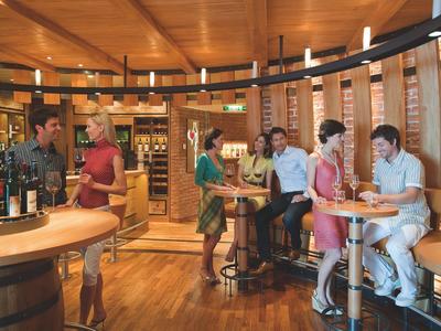 Gemütliche Weinbar mit Holzinterieur, mehreren Gästen und Weinflaschen auf Tresen und Regalen.
