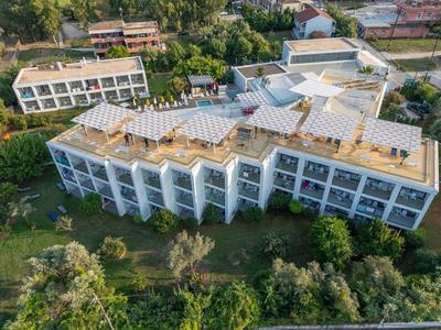 Mehrstöckiges weißes Gebäude mit Flachdach und Solarpanels, umgeben von Bäumen und Grünflächen.