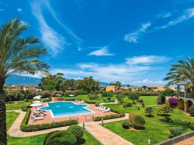 Beautiful hotel garden with pool, palm trees and lounge chairs under blue sky