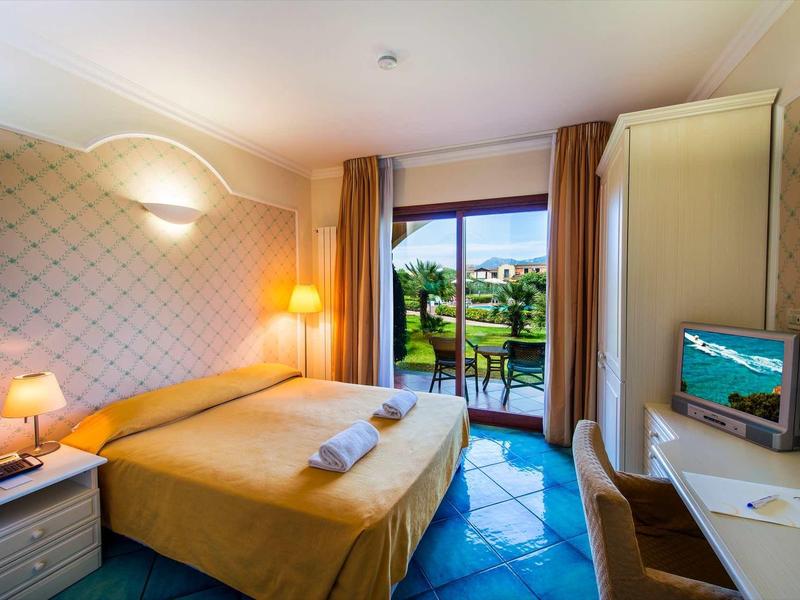 Bright hotel room with double bed, desk, and view of garden and pool.