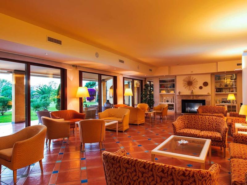 Bright hotel lounge with armchairs, sofas, and large windows overlooking the garden.