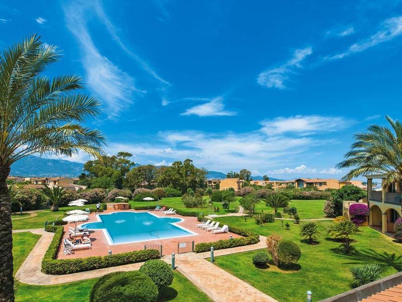 Beautiful hotel garden with pool, palm trees and lounge chairs under blue sky
