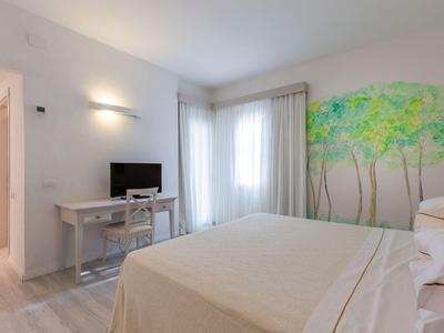 Helles Hotelzimmer mit Doppelbett, Tisch mit Stühlen, TV und Wandbild mit Bäumen.