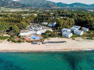 Luftaufnahme eines Resorts am Strand mit Pool, Sonnenschirmen und Bergen im Hintergrund.