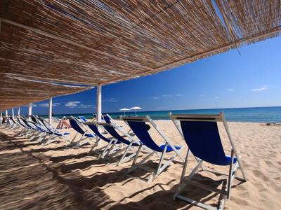 Reihe von blauen Liegestühlen unter einem Strohdach am Sandstrand mit Blick auf das Meer.