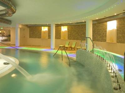 Innenpool mit warmem Licht, Whirlpool und Sitzgelegenheiten in einem modernen Spa-Bereich.