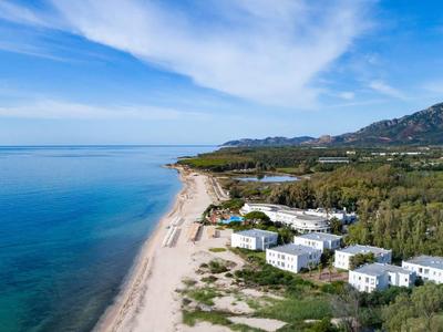 Blick auf weiße Gebäude an einem langen Sandstrand mit blauem Meer und bewölktem Himmel.