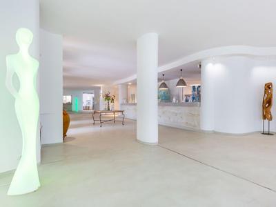 Heller und moderner Hotellobby mit weißen Wänden, Skulpturen und einem Empfangstresen.