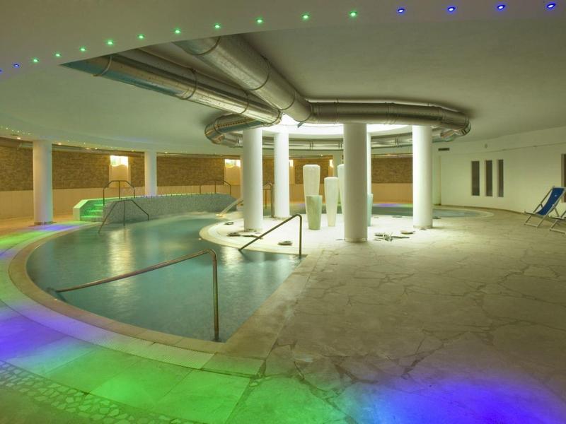 Moderner Innenpool mit geschwungenem Becken, Lichtakzenten und Liegestühlen am Rand.