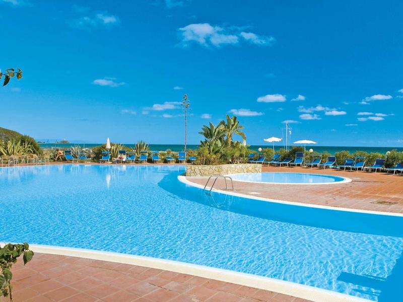 Großer Außenpool mit blauem Wasser, umgeben von Terrakottafliesen und Blick auf das Meer.