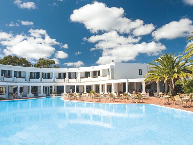 Moderner Hotelkomplex mit großem Schwimmbad und Palmen bei sonnigem Wetter.