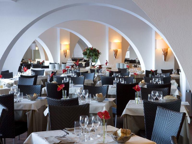 Elegantes Restaurant mit weißen Bogenwänden, gedeckten Tischen und dunklen Stühlen, stimmungsvolle Beleuchtung.