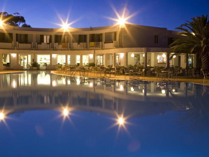 Hotelgebäude mit Beleuchtung spiegelt sich in großem blauem Pool bei Dämmerung wider.